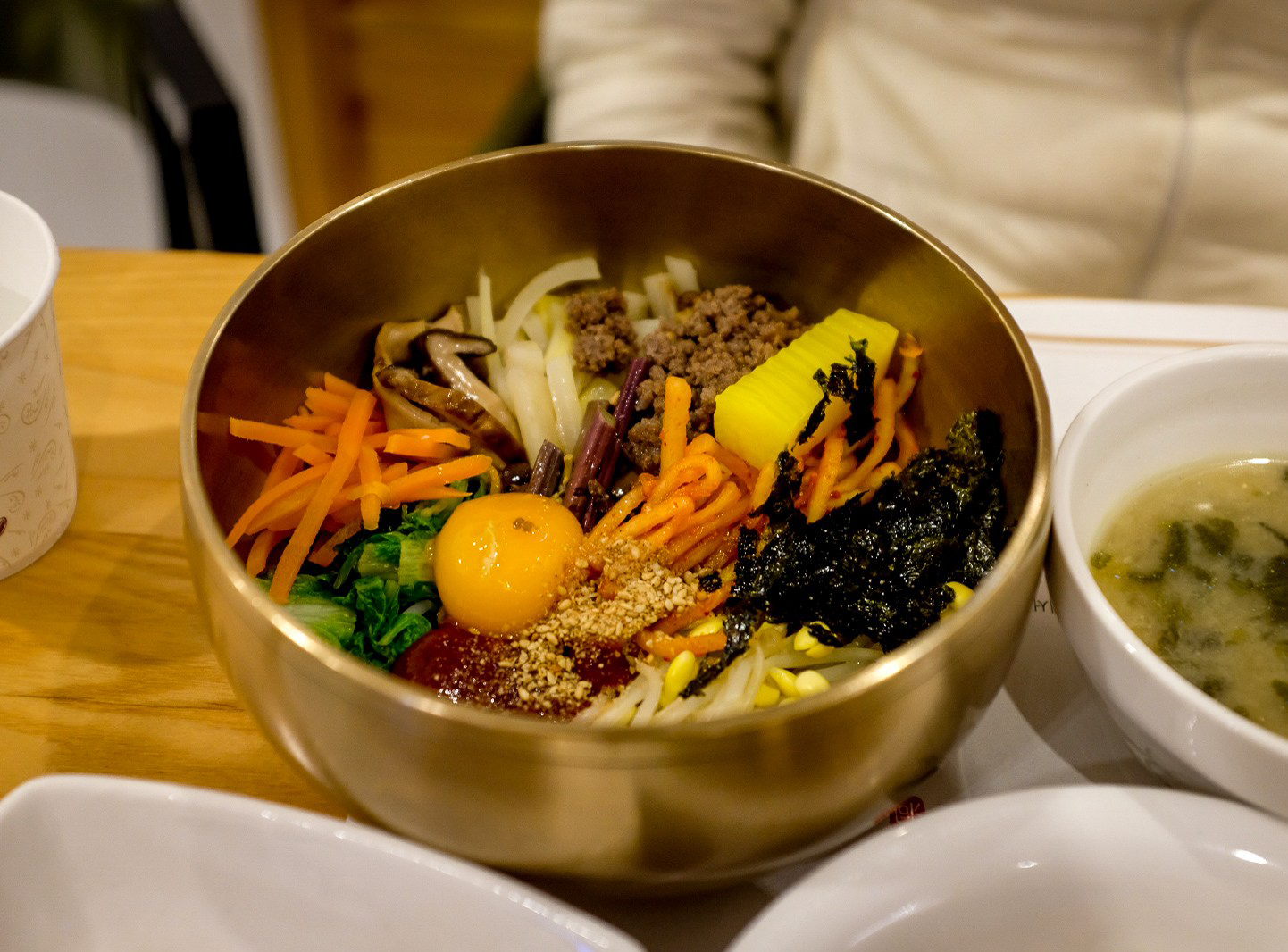 Copper bowl of rice with seasoned vegetables, sliced meat and chili pepper sauce